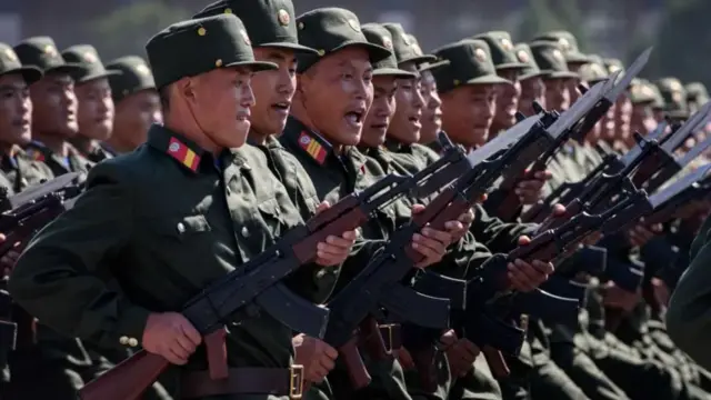 North Korean troops lined up with guns cocked, wearing green uniforms and hats