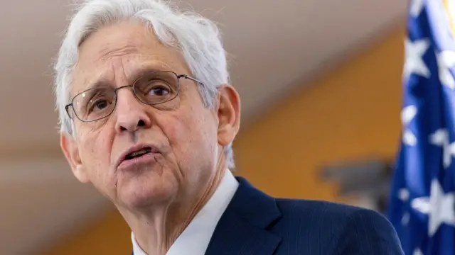 A grey haired man with glasses in a blue suit