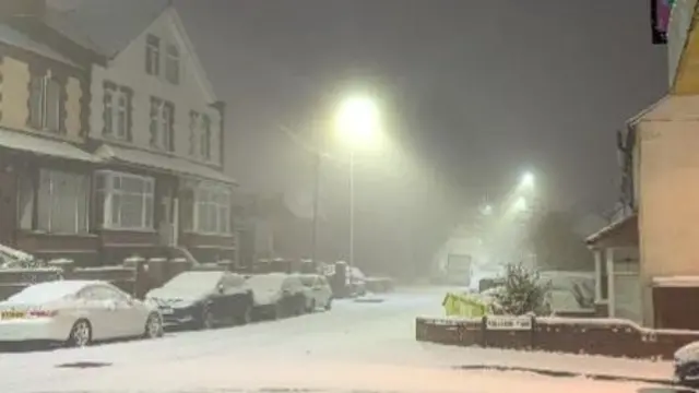 A snowy street with cars parked alongside a row of houses