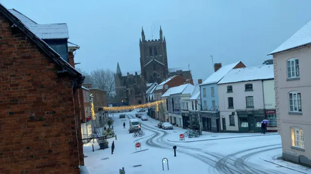 A view of a snow-covered shopping street with a string of Christmas and a church in the background.