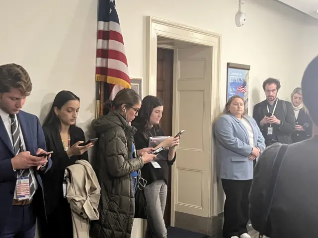 People standing outside a doorway looking at phones