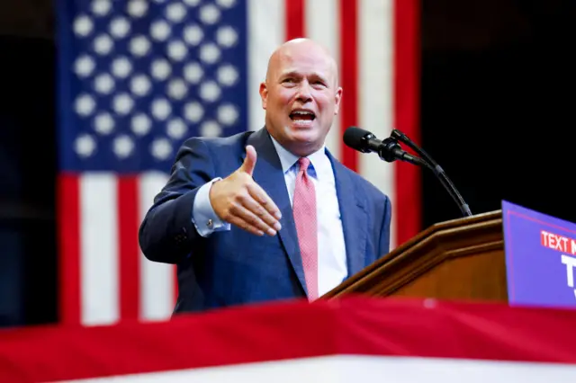 Bald man in blue suit speaks at microphone and gestures his right hand