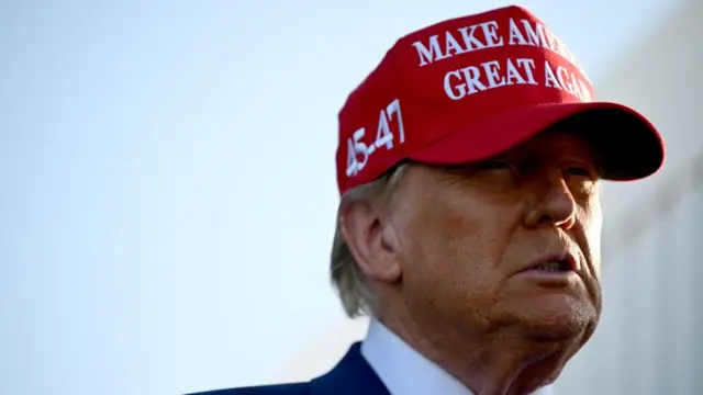 Donald Trump looks out wearing a red 'Make America Great Again' cap.