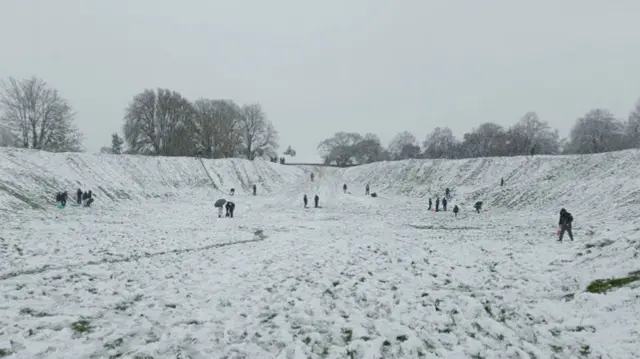 A wide shot of people playing on a thin layer of snow with embankments on either side