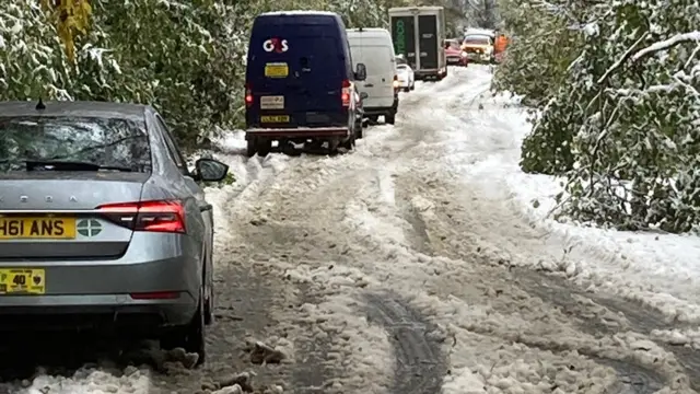 Cars and vans queue in a snowy lane.