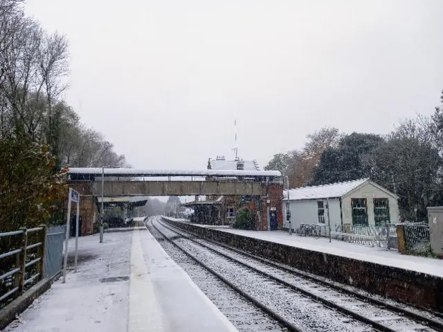 A snowy scene at a railway station with the platform covered in snow