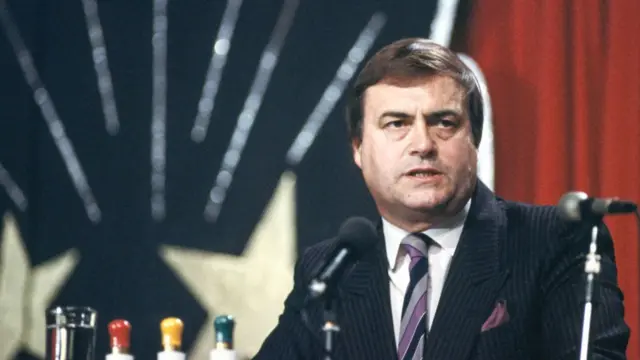 John Prescott at a National Union of Mineworkers meeting in 1998. He's in black pin-striped suit, white shirt and striped black, grey and purple tie. Blurred union flag in the background