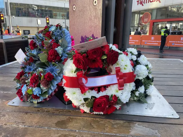 A close-up of wreaths laid at the memorial decorated with red and white flowers