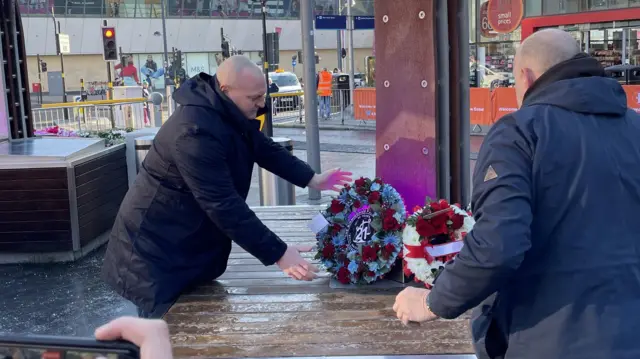 Fans lay two wreaths, decorated with red and white flowers, at the memorial