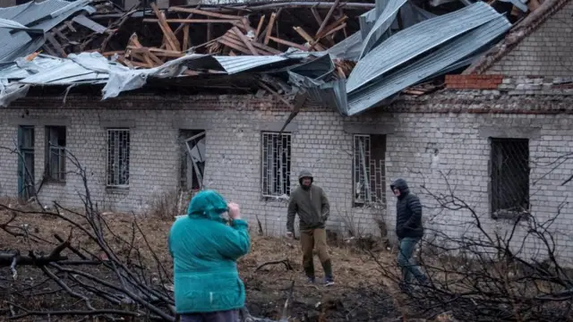 Residents walk at a site of a Russian missile strike, amid Russia's attack on Ukraine, in Dnipro, Ukraine. The roof is torn up and there are people taking pictures as they survey the damage of a brick building.