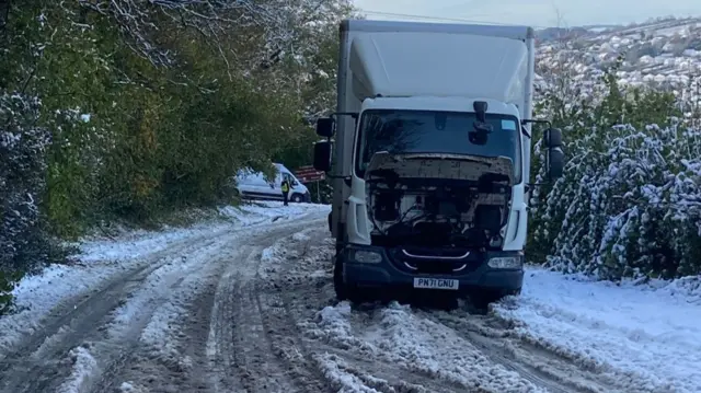 A lorry with its engine cover open on a snowy road.