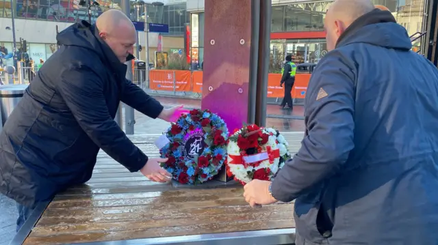 Matt Glover laying his wreath at Birmingham New Street. He has his arms stretched out and you can see the wreath.