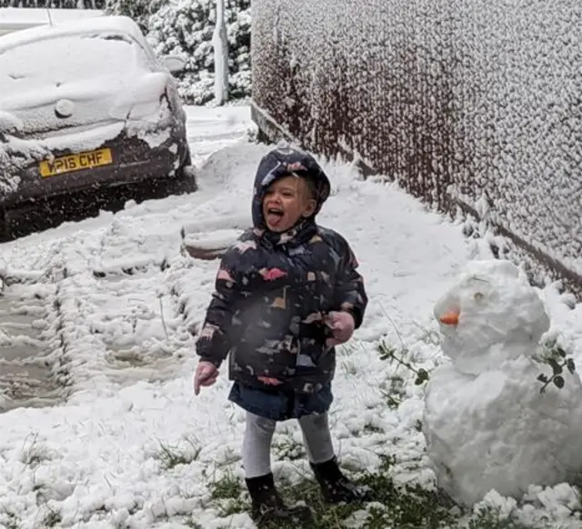 A small girl in boots and anorak with her tongue out with snow on the ground