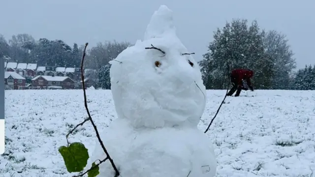 A snowman in a snowy park with twig arms.