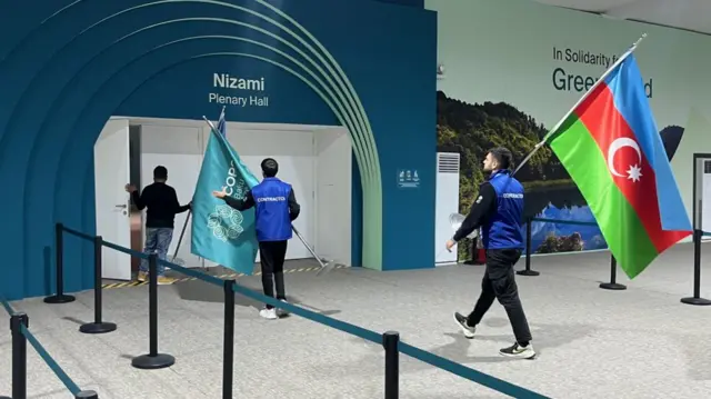 Two workers carrying large COP29 and Azerbaijan flags into the hall.