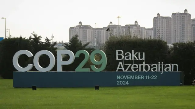 Reuters A COP29 sign on a patch of grass with a backdrop of the cityscape in Baku, Azerbaijan showing several tower blocks.