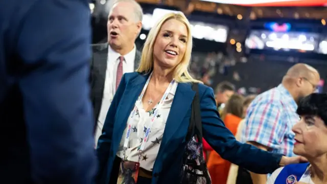 A blonde woman in a navy jacket holds her hand on another woman's shoulder