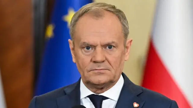 Polish Prime Minister Donald Tusk attends a press conference, staring straight into the camera wearing suit