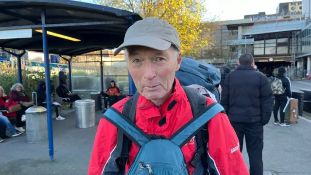 A man in a red jacket with a blue rucksack attached to his front.