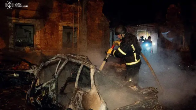 A firefighter spraying water over burnt-out car