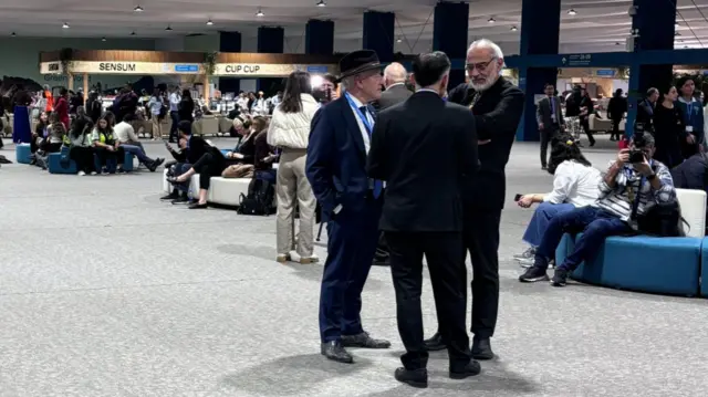 Three men in suits stood in a corridor, discussing something