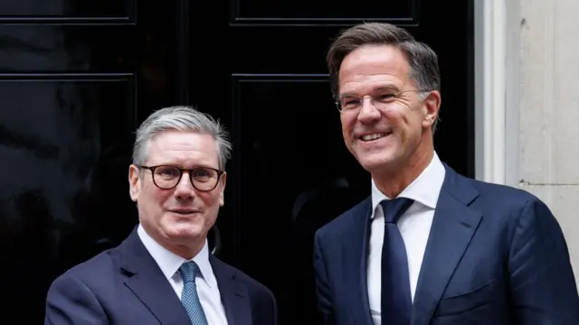 Keir Starmer and Mark Rutte stood in front of a black door. Both are wearing suits, smiling.