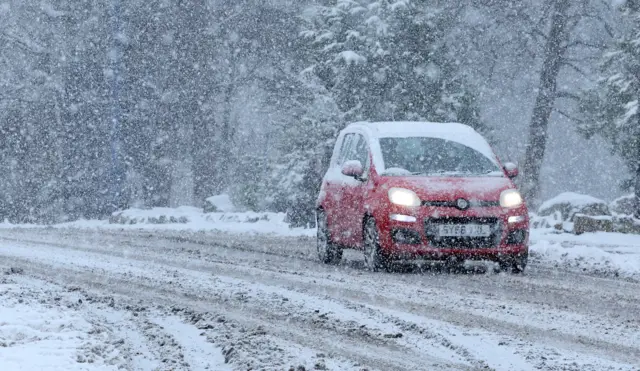 a red car drives through snow on a road in Aviemore