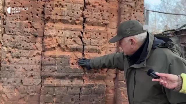 Sumy regional administration chief Volodymyr Artyukh touching a brick wall covered in holes