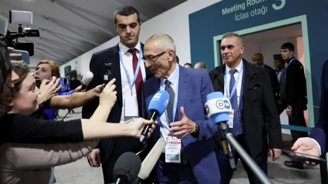 US advisor John Podesta gestures as he is surrounded by journalists holding microphones towards him