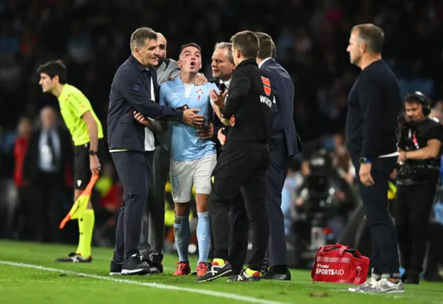 Aspas is held back by a coach as he shouts at the officials on the touchline