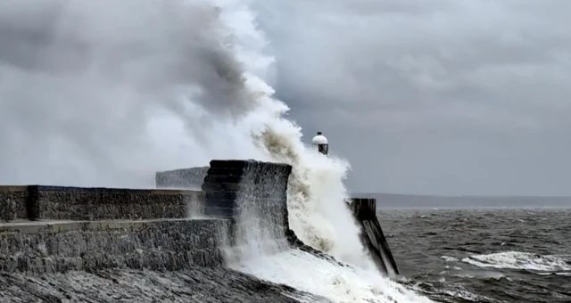 Waves crash against a pier in Wales, with dark grey sky above