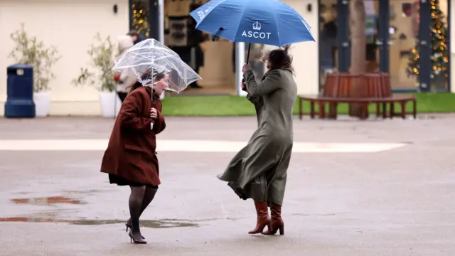 Two women wrestle with their umbrellas during a windy day at Ascot Racecourse.