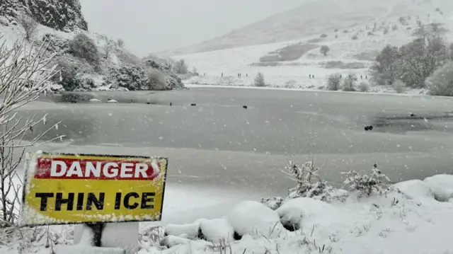 A warning sign reads: "Danger thin ice" ar the loch. There are flakes of snow.