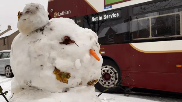 Snow man in front of a bus