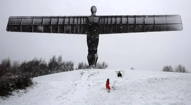 Angel of the North sculpture in Gateshead covered in snow with two people sledging down the hill under the sculpture