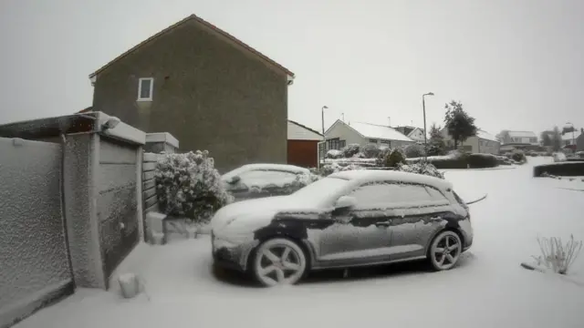 Snow covers a cars and blankets the street.