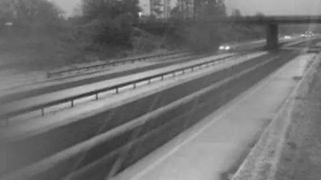 The black and white image shows carriageways of the M9. Snow is falling at there is snow at the side of the road.