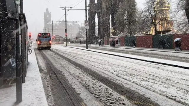 Snow and slush covers a road. The bottom of the Sir Walter Scott monument is visible and a bus at the top of the road.