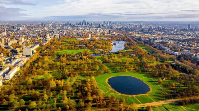 Autumnal aerial shot of Hyde Park from the Kensington side - the Serpentine and pond are visible as is the London skyline in the background