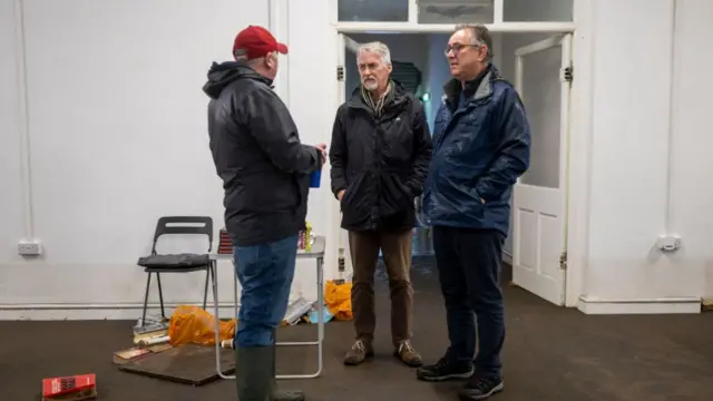 Deputy first minister irranca-davies (centre) listens to Pontypridd resident during his visit. He's wearing a dark green rain jacket, beige corduroy trousers and brown trainers