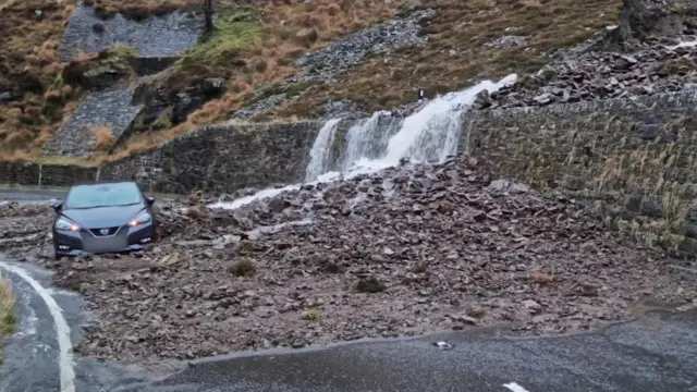 A car affected by a landslip on a road in Wales