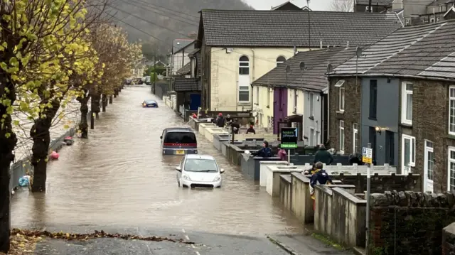 Flooding in Pontypridd, Wales. Three parked cars can be seen partially submerged underwater in front of two-floors terraced houses