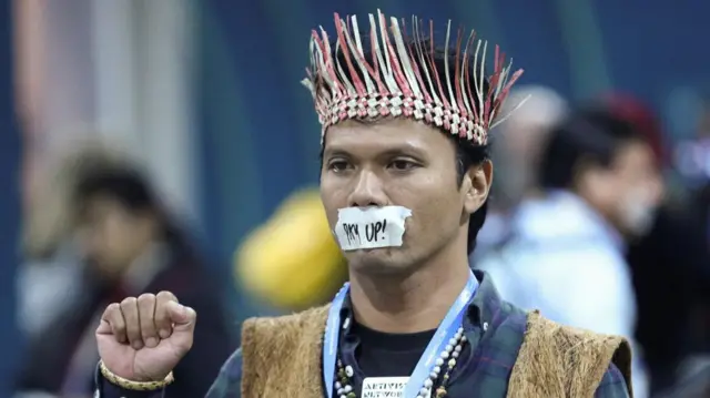 An environmental activist with his mouth taped raises his first.