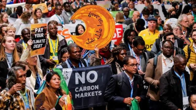 A crowd of environmental activists with signs "pay your climate debt" and "no carbon markets".