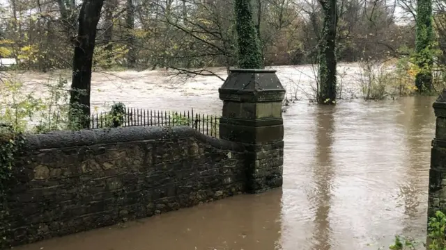 The River Taff flooding in Wales, with high water levels shown rising up against trees and a wall