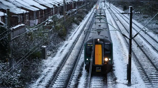 Train passes over snow-covered tracks next to terraced houses near Liverpool