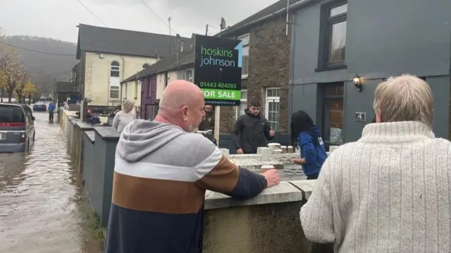 Residents on a flooded street in Rhondda. Ca cafe is handing out coffees