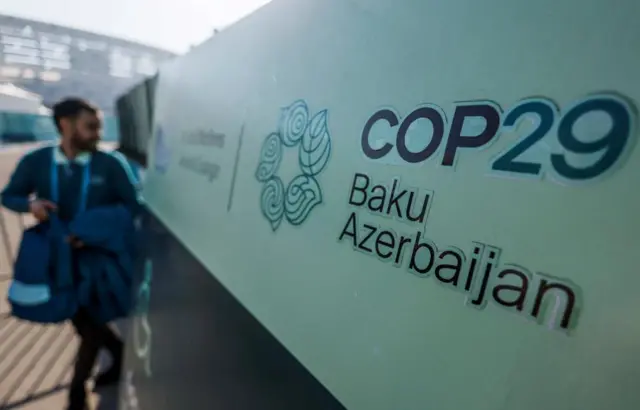 Close up of COP29 outdoor sign, with words Baku Azerbaijan and the logo, with a man out of focus on far left