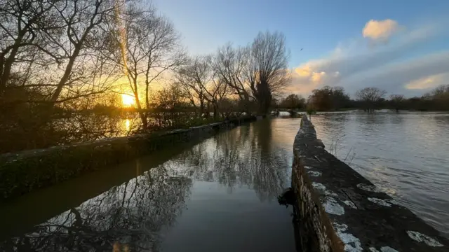 Setting sun with orange and blue sky, with whispy clouds, over floodwater