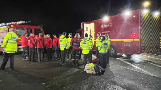 Emergency service crew standing on a road with fire service vehicles around them